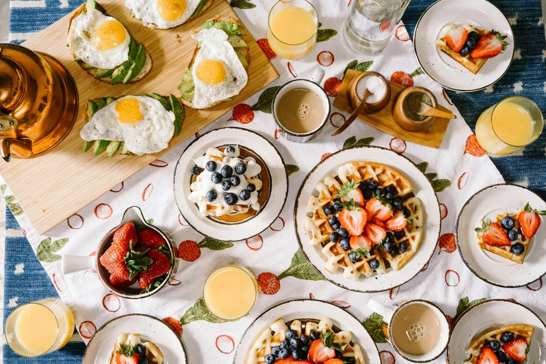 A breakfast table spread with waffles, eggs, fruit and juice, seen from above
